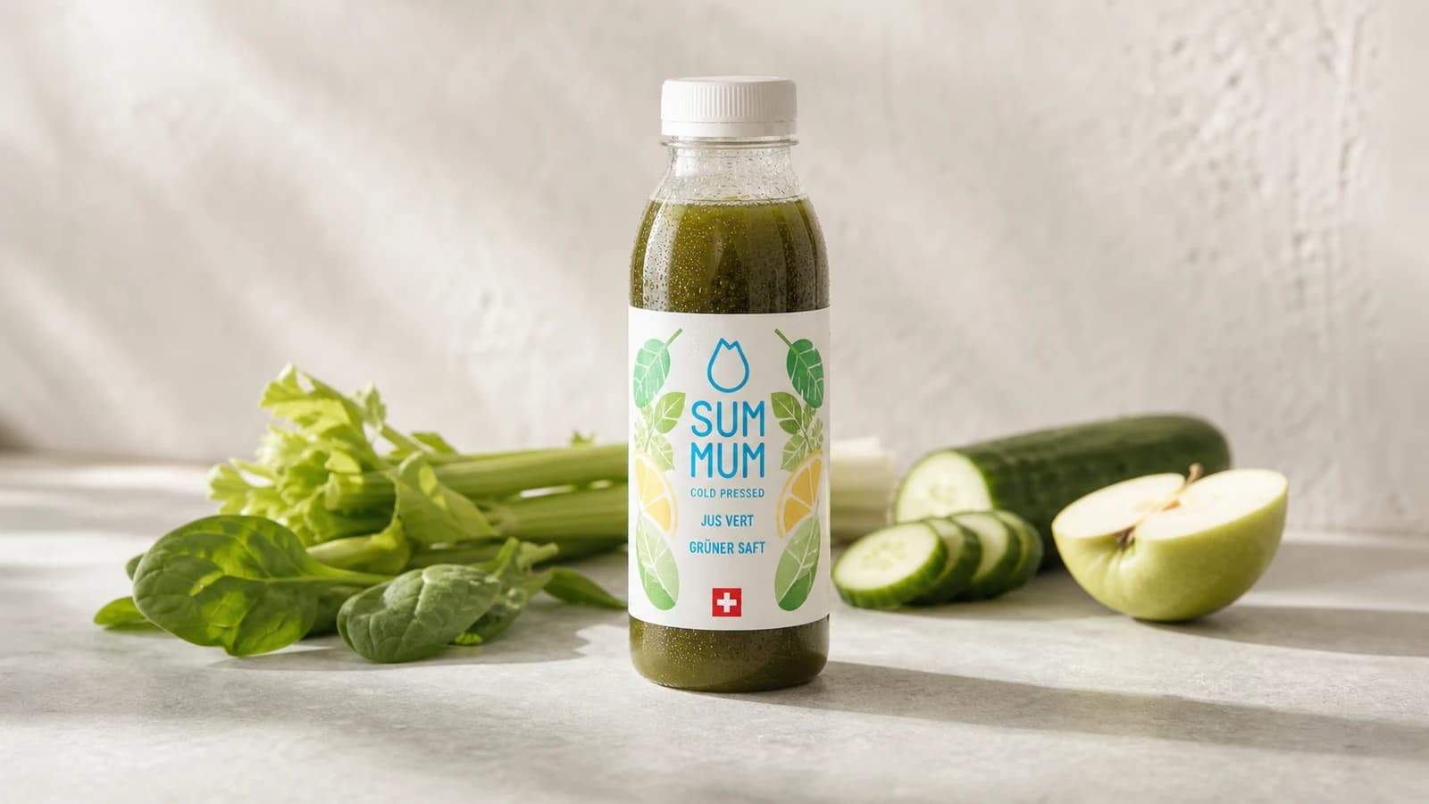 Bouteille SUM MUM Jus Vert pressée à froid sur fond ivoire, légumes verts frais — épinards, céleri, cresson — en composition sobre