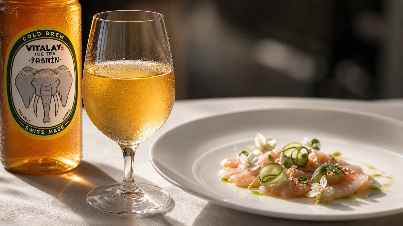 Verre de thé froid Jasmin Vitalay à côté d'une assiette de restaurant dressée, lumière chaude de salle