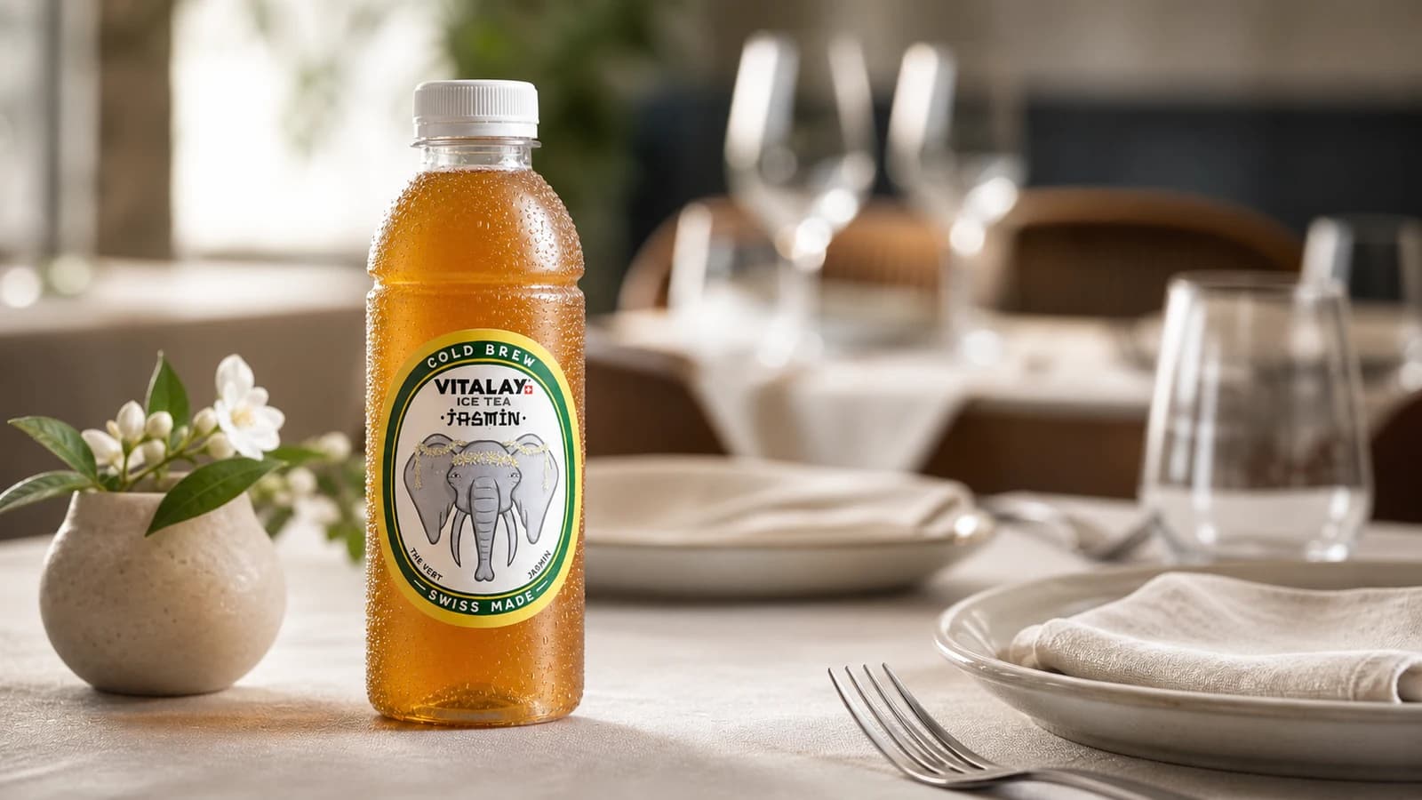 Bouteille Vitalay Thé froid Jasmin sur table de restaurant dressée, couverts et verre eau en fond flou