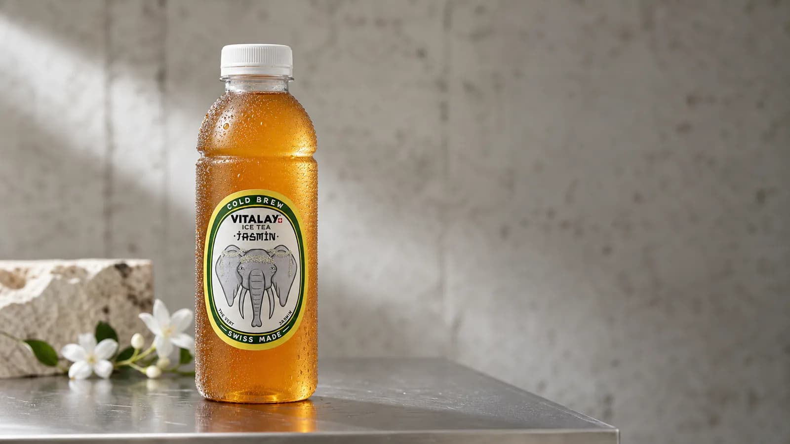 Bouteille Vitalay Jasmin couverte de condensation sur inox brossé, lumière d'atelier suisse