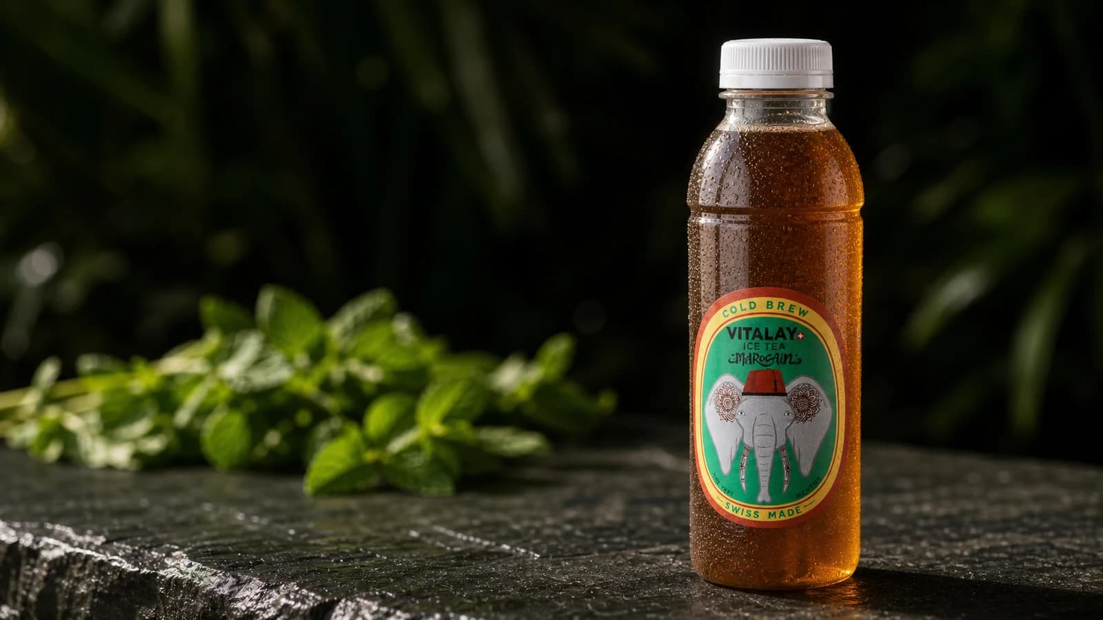 Bouteille Vitalay Thé froid Marocain posée sur pierre, feuilles de menthe fraîche en arrière-plan flou